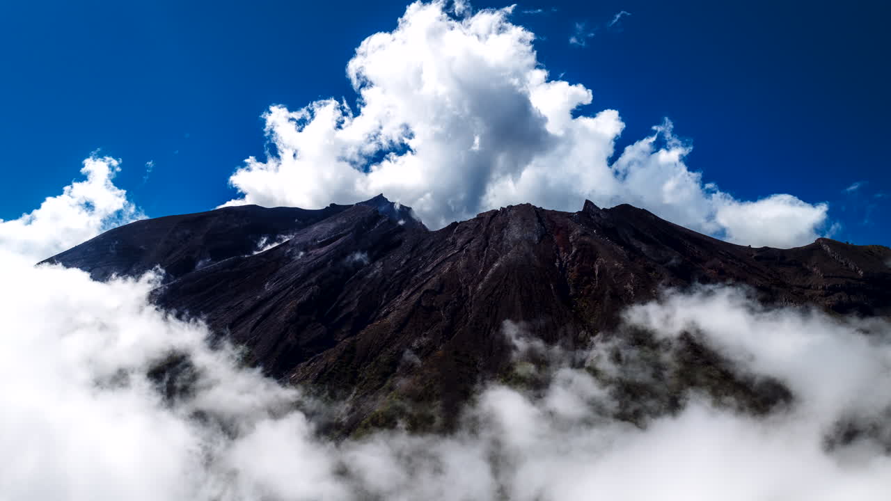 nubes blancas y brumosas rodando sobre el monte agung, indonesia, colores azules vívidos y cima oscura de la montaña