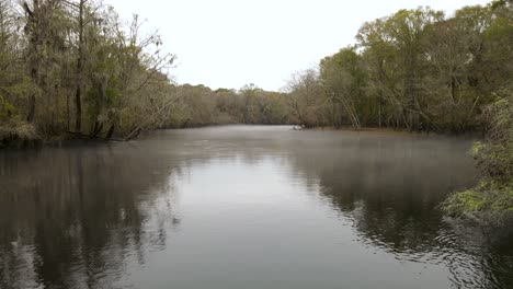 Leichter-Nebel-Bedeckt-Einen-Dunklen,-Ruhigen-Fluss-Und-Ein-Umgestürzter-Baum-Blockiert-Den-Fluss