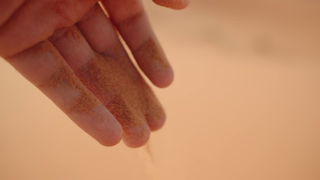 Golden Sahara sand trickles between fingers, drifting gently in warm light