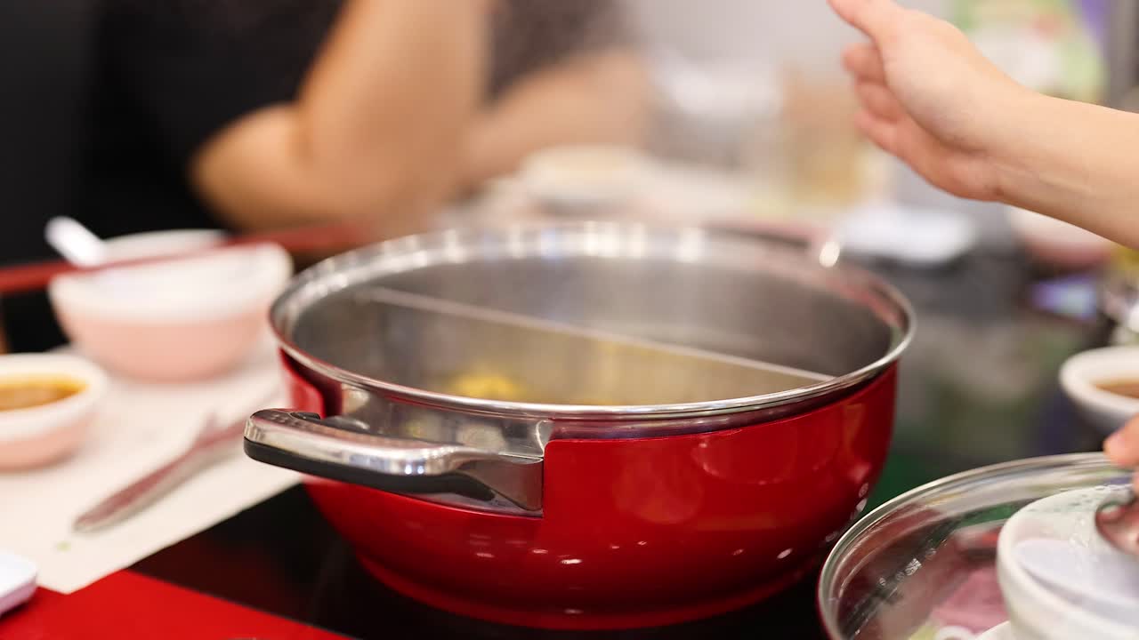 manos preparando una olla caliente en una mesa de comedor