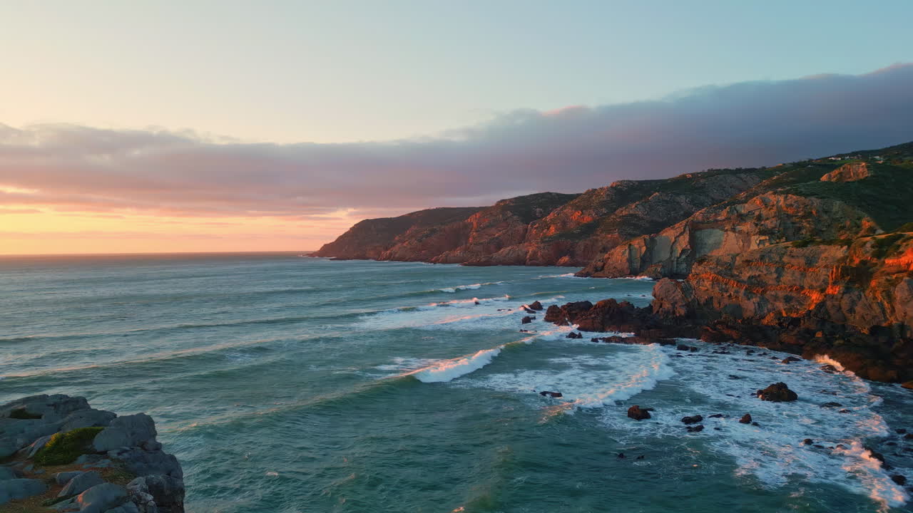 Vista aérea de falésias vulcânicas encontrando o oceano ao pôr do sol. Mar espumante na costa.