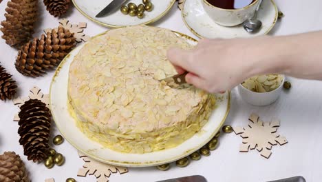 housewife cut off piece of homemade cake with almond petals on white wooden table.