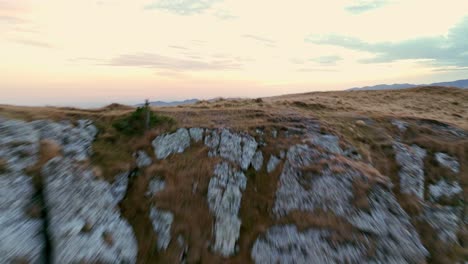 Aerial-forward-flight-over-rocky-cliff-showing-beautiful-forest-trees-and-mountain-range-in-background