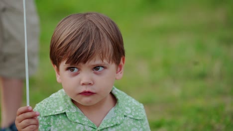 portrait of adorable small baby boy outdoors. cute child is sitting on the grass and eating from spoon in summer day.