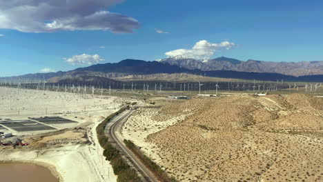 drone vuela sobre las vías del tren hacia la granja de molinos de viento en palm springs, montañas de san bernardino en la distancia