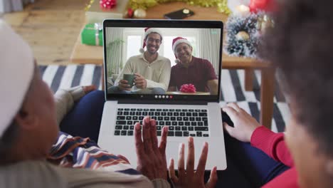 African-american-mother-and-daughter-using-laptop-for-christmas-video-call-with-family-on-screen