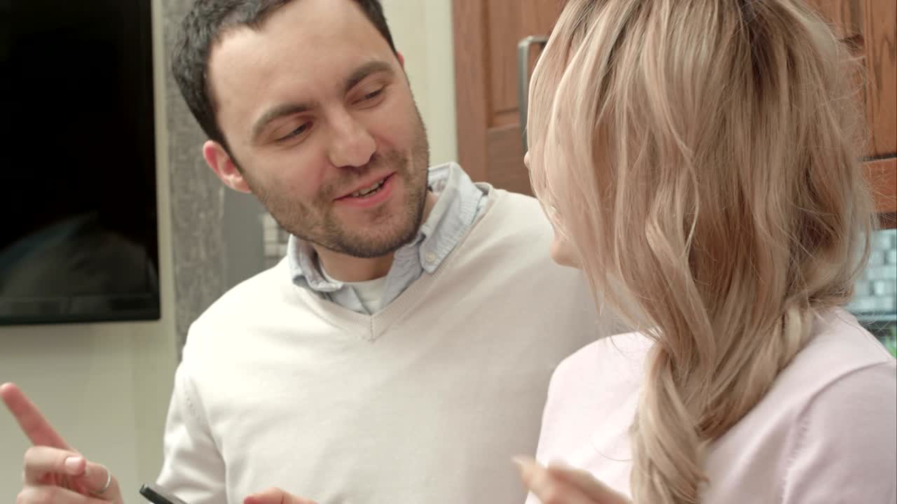 Young couple listening to music via smartphone, talking in the kitchen