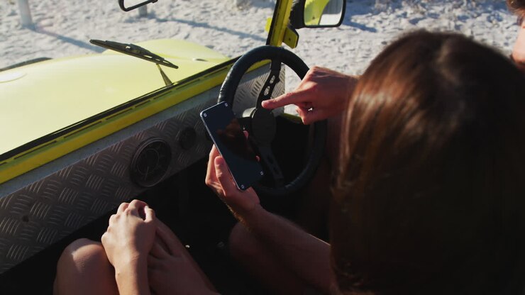 Una felice coppia caucasica seduta in un buggy sulla spiaggia vicino al mare usando uno smartphone