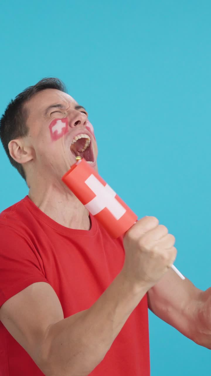 Man cheering for Switzerland waving a national flag looking away