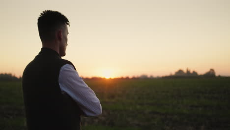 A-man-farmer-looks-into-the-distance-at-his-field,-stands-alone-at-sunset.