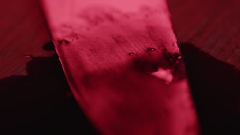 extreme close up of a blood covered knife in a puddle of blood while red and blue police lights illuminate the crime scene