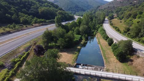 Luftaufnahme-Eines-Flusses,-Der-Zwischen-Autobahnen-In-Einer-Bergigen-Gegend-Eingeklemmt-Ist