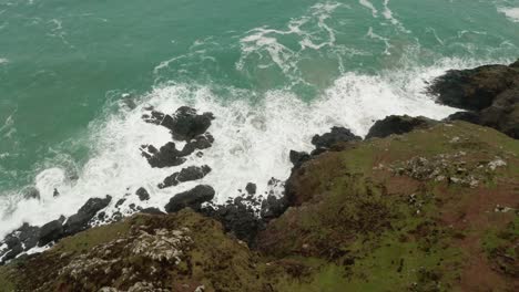 Aerial-tilt-up-from-the-crashing-waves-at-land's-ends-to-the-open-Atlantic-Ocean