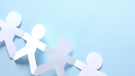 Close-up-of-people-holding-hands-made-of-white-paper-on-blue-background-with-copy-space