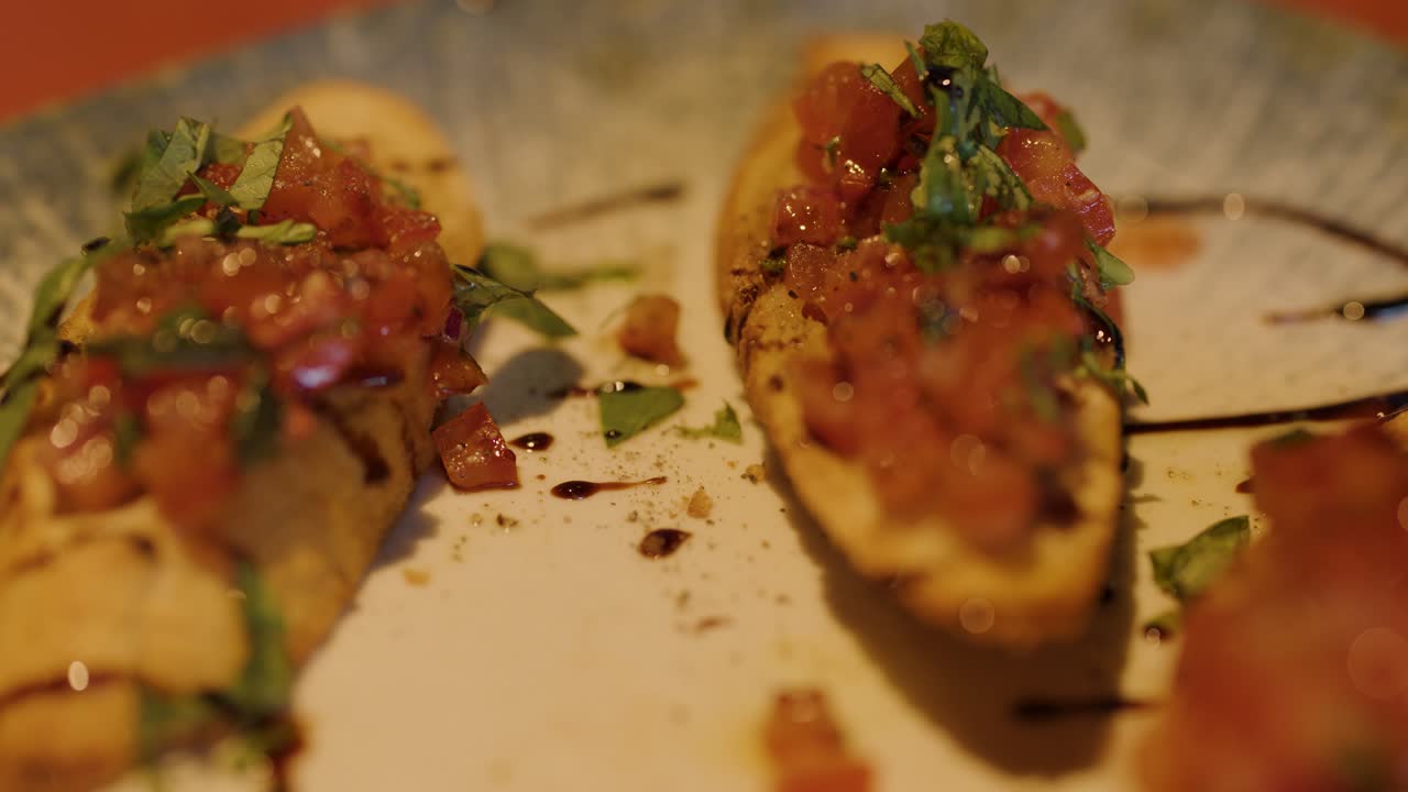 A hand grabs bruschetta from a ceramic plate under warm, ambient lighting with shallow focus