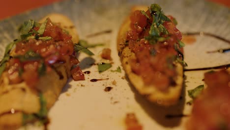 A hand grabs bruschetta from a ceramic plate under warm, ambient lighting with shallow focus