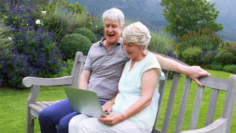 Senior-couple-talking-and-using-laptop-on-bench