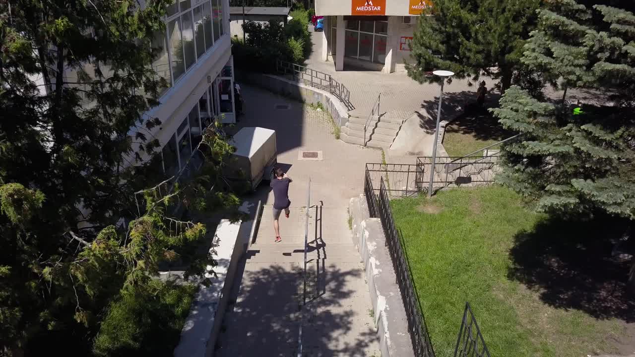disparo aéreo de un dron siguiendo a un joven corredor libre de parkour macho adulto volteando y saltando por tramos de escaleras