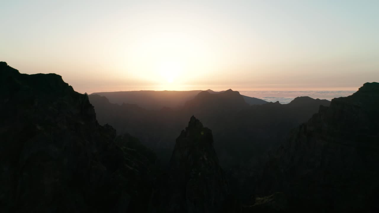 Lowering aerial of bright sunset with silhouette mountain peaks of Madeira