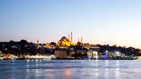 zoom out timelapse view of istanbul cityscape with suleymaniye mosque with tourist ships floating at bosphorus at night