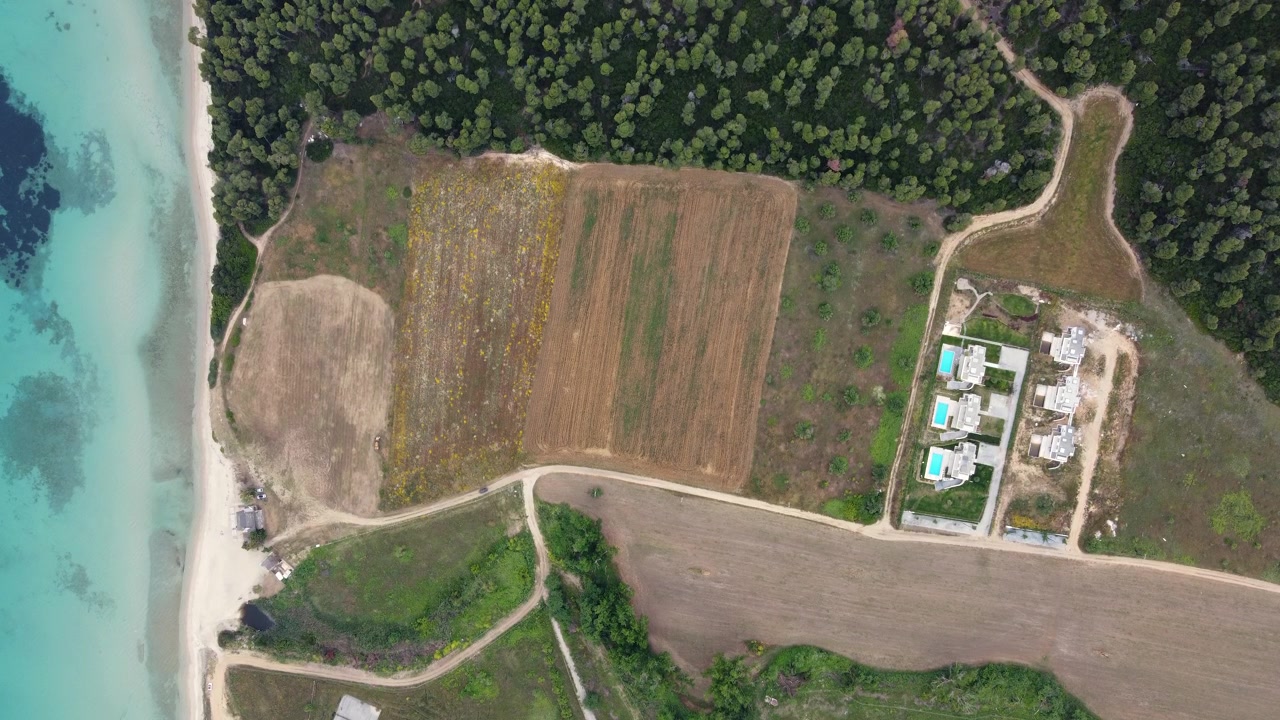 Aerial View of Car Driving Toward a Turquoise Seashore Beside Farmland and Villas in Kassandra Greece, Birds Eye View