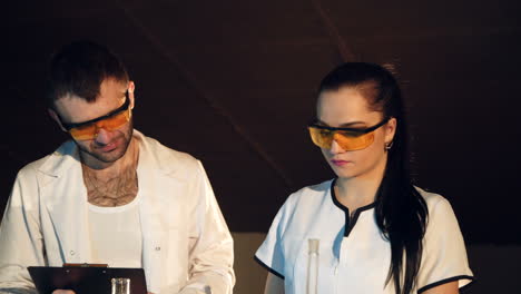 two scientists are working in laboratory. young female and male researcher are doing investigations with test tubes.