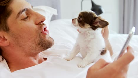 young man lying on bed stroking his puppy while using mobile phone 4k 4k