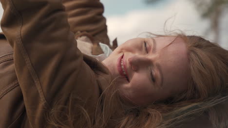 Portrait-Of-A-Beautiful-Smiling-Red-Haired-Woman-Lying-Outdoors-Looking-Directly-At-The-Camera