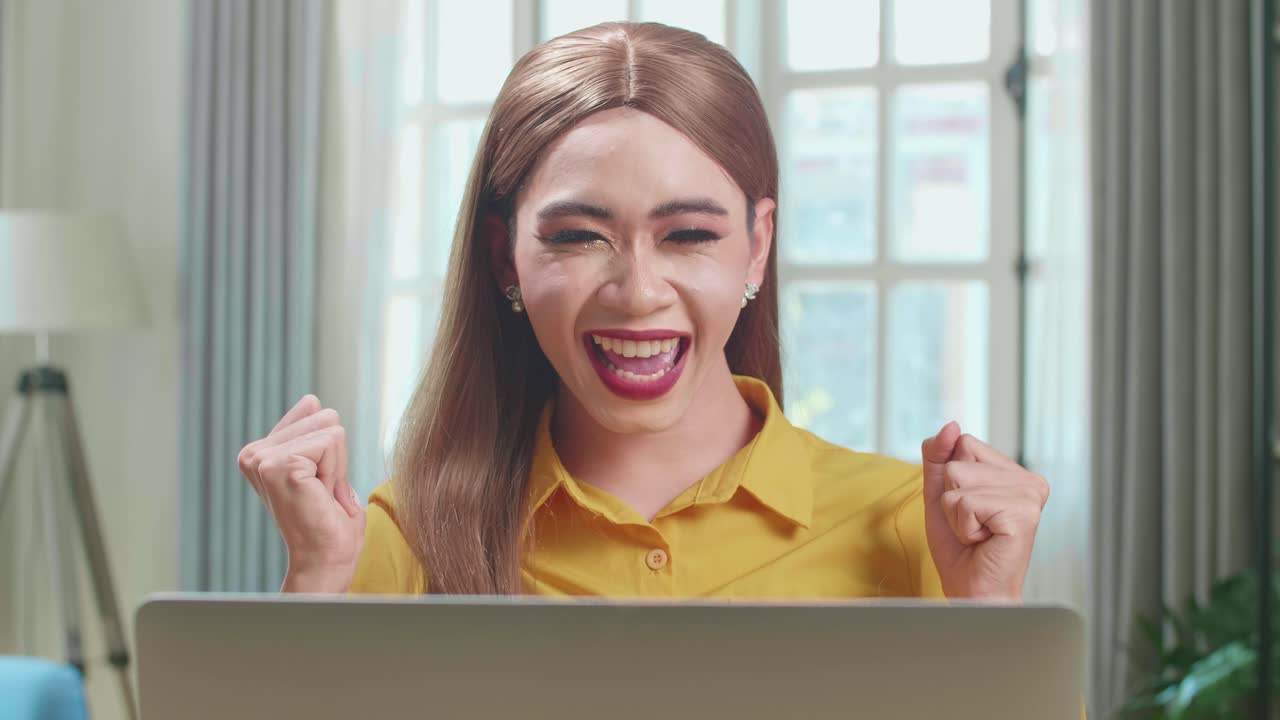 Asian Young Transgender Woman Working With Laptop Computer And Celebrating In Living Room