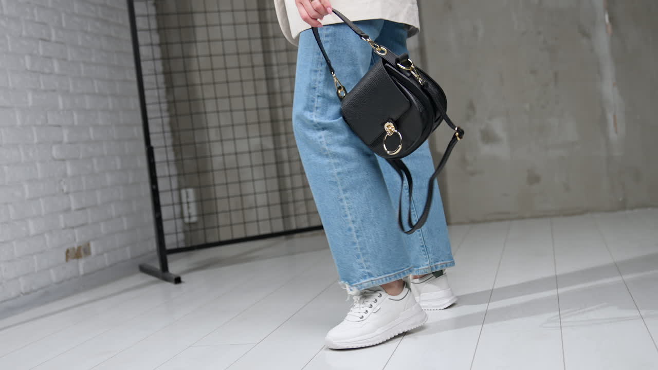 Fashionable casual style for females. Jacket, jeans, white sneakers and black leather bag. Studio footage.