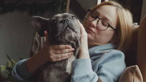 Close-Up-View-Of-Red-Haired-Woman-Caresses-Her-Bulldog-Dog-While-They-Are-Sitting-On-The-Sofa-In-The-Living-Room-At-Home