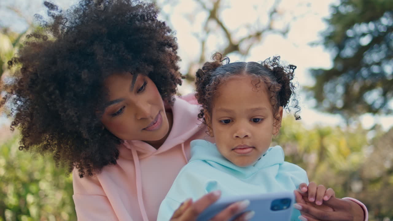 niño lindo viendo dibujos animados en el teléfono en las manos de la madre al aire libre de cerca.