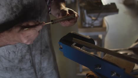 midsection of caucasian male knife maker in workshop using sander