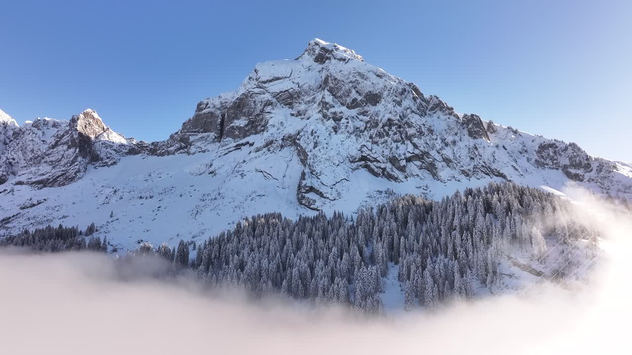 Aerial view of Fronalpstock's snow-capped peak emerging through a sea of fog, set in the serene landscape of Glarus, Switzerland.