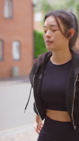 video vertical de una mujer joven haciendo ejercicio corriendo por una calle urbana usando auriculares inalámbricos filmado en tiempo real 3