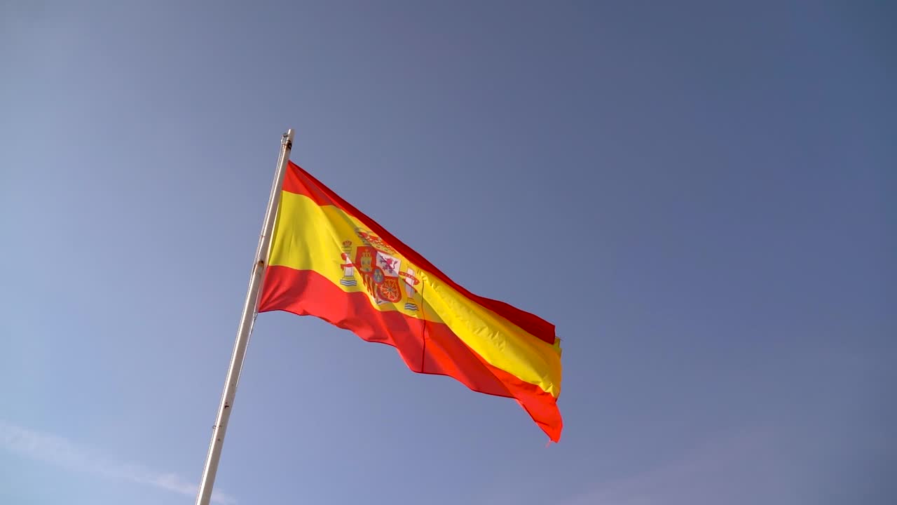 Bandeira Nacional da Espanha tremulando contra o céu azul em tempo ventoso
