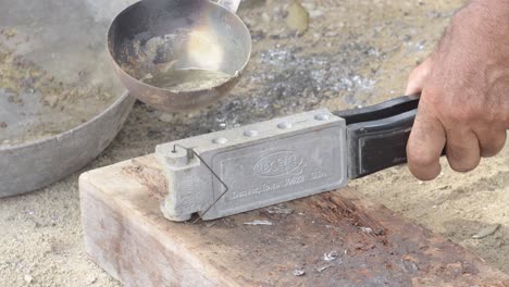 close-up of molten lead being poured into a mold by a person's hand, craftsmanship in action