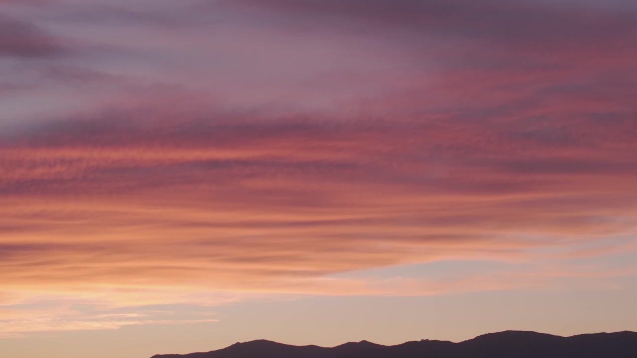 Telephoto drone pan from right to left capturing the dark mountain skyline of the Central Mountain Range beneath glowing yellow, orange and red sunset clouds above the Tiétar Valley.