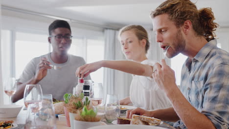 grupo de amigos jóvenes sentados alrededor de la mesa en casa disfrutando de la comida juntos