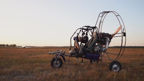 el parapente de motor se encuentra en el aeropuerto en los rayos de la luz del atardecer. en el fondo, el avión despega. la cámara se mueve a lo largo de la órbita