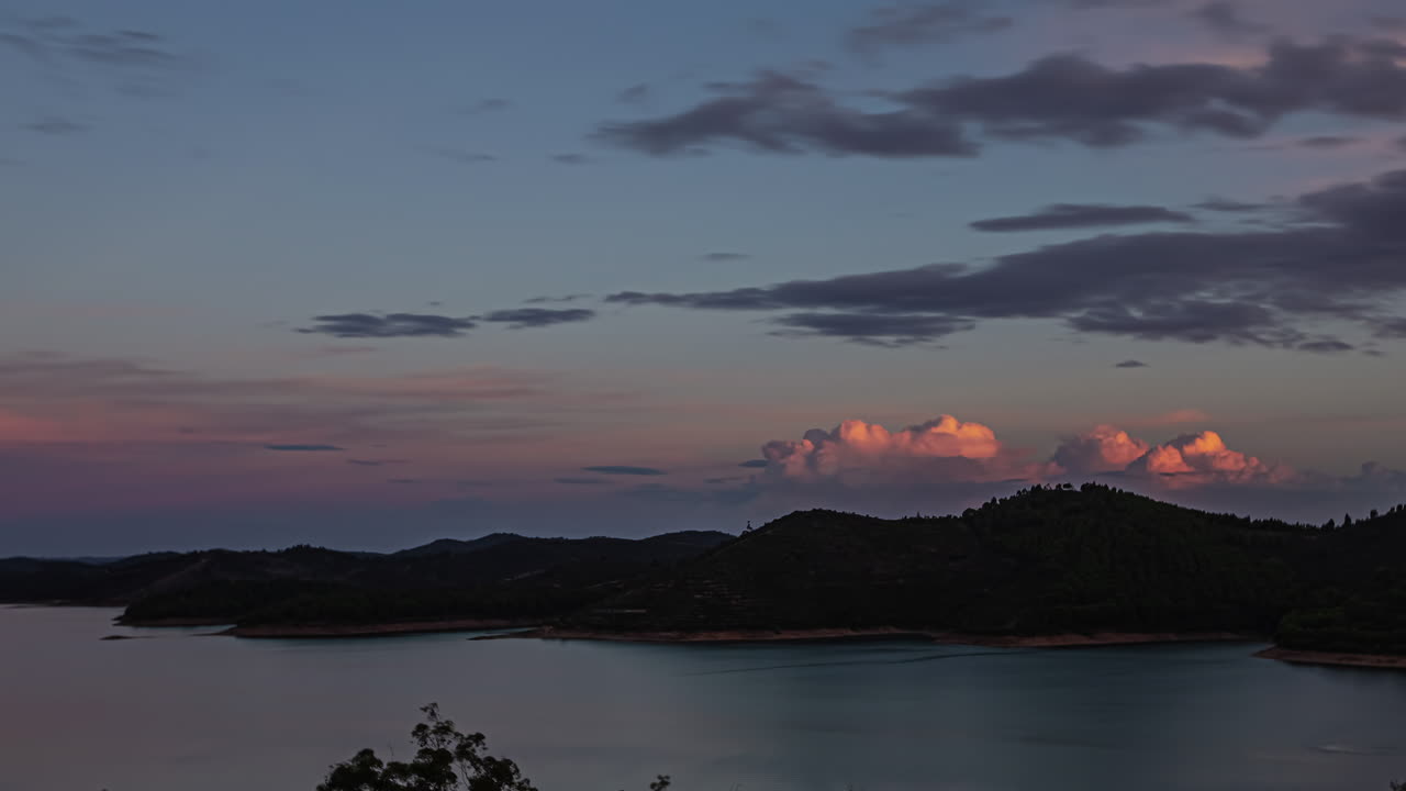 cielo al amanecer con nubes naranjas que avanzan sobre un lago y montañas