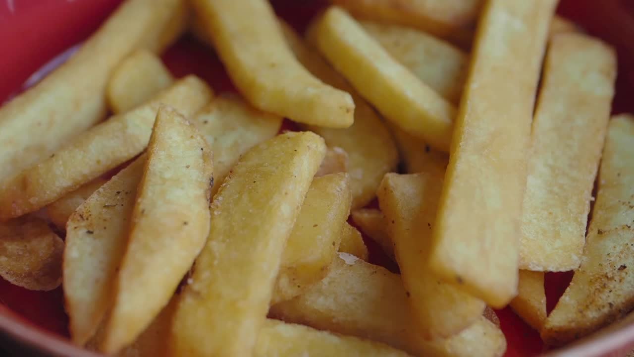 cerca de una mano recogiendo papas fritas de un plato rojo
