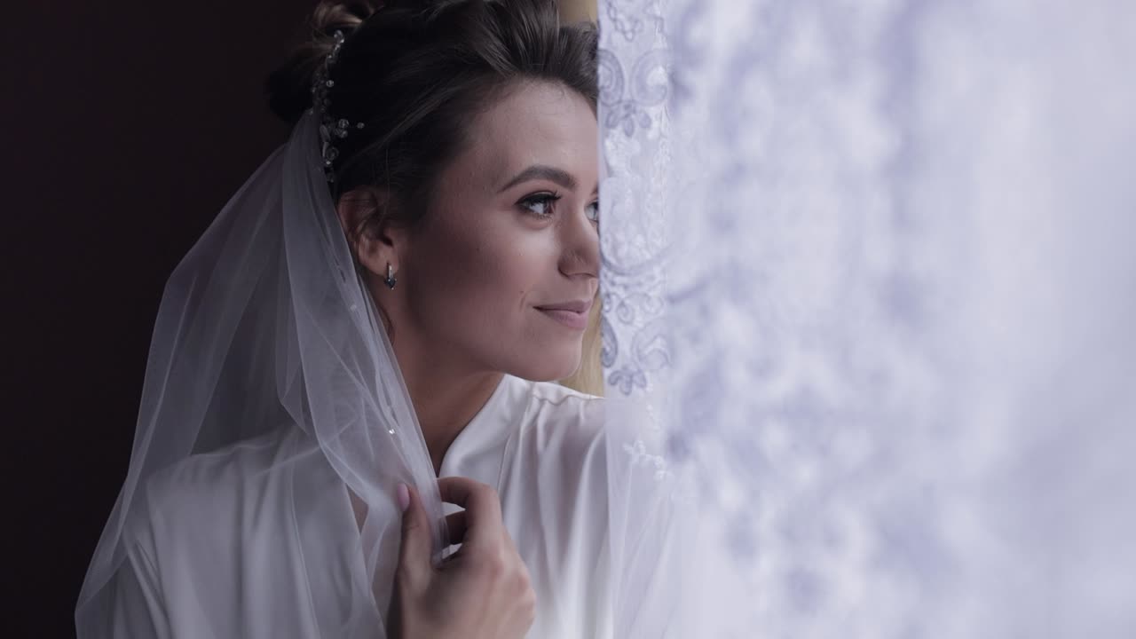 Noiva em vestido boudoir perto da janela, preparativos matinais do casamento, mulher em camisola e véu.