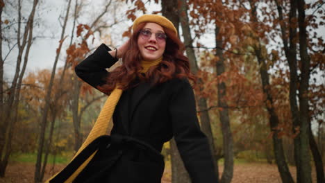 mujer alegre con abrigo negro y boina amarilla juega en las hojas de otoño, girándose con una sonrisa, capturando la esencia del espíritu lúdico del otoño