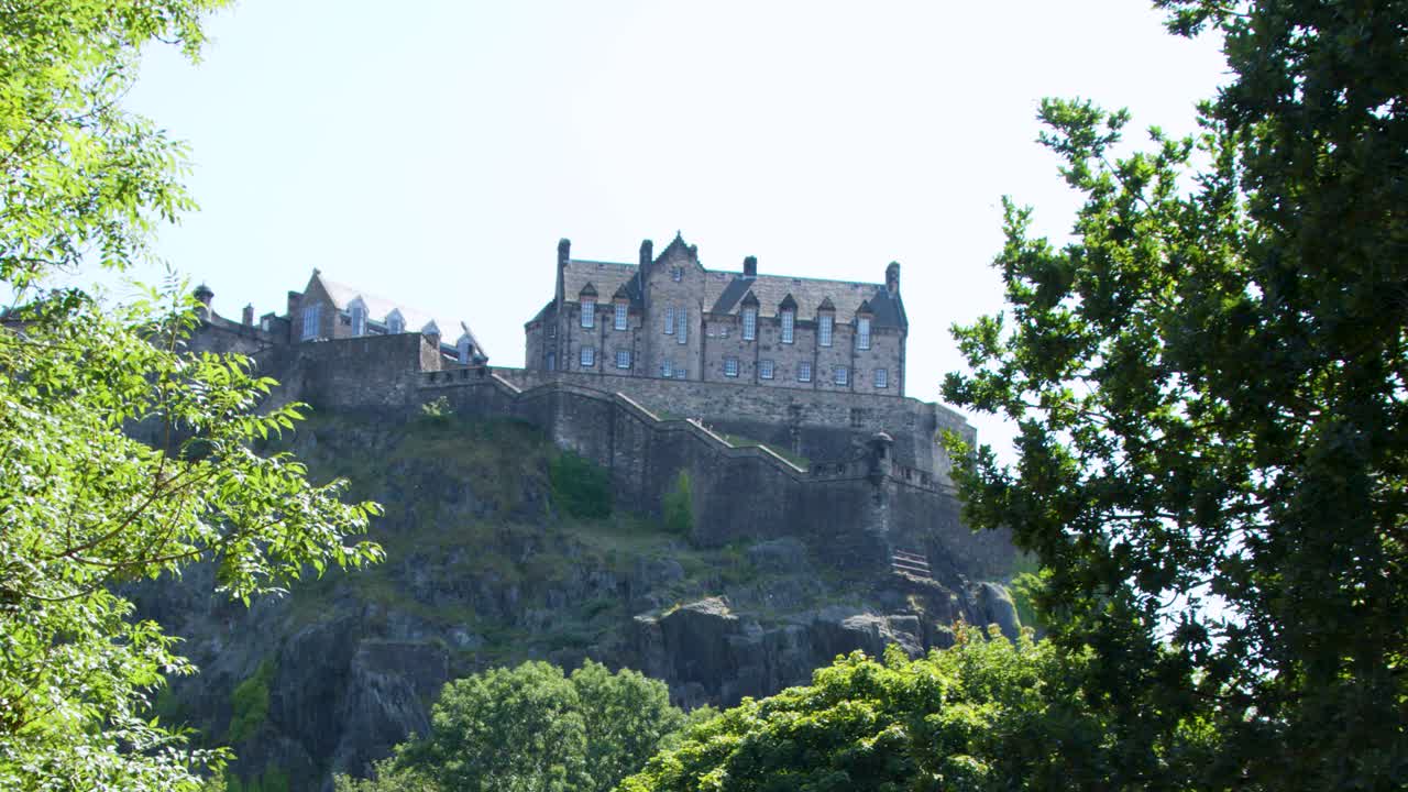 Camera pans across Edinburgh castle behind leafy trees, bright daylight, clear summer atmosphere