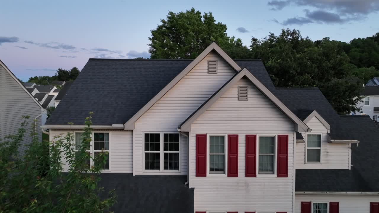 Charming suburban home with welcoming porch, framed by trees. The well-maintained yard and inviting architecture reflect American family life. Aerial approaching flight.