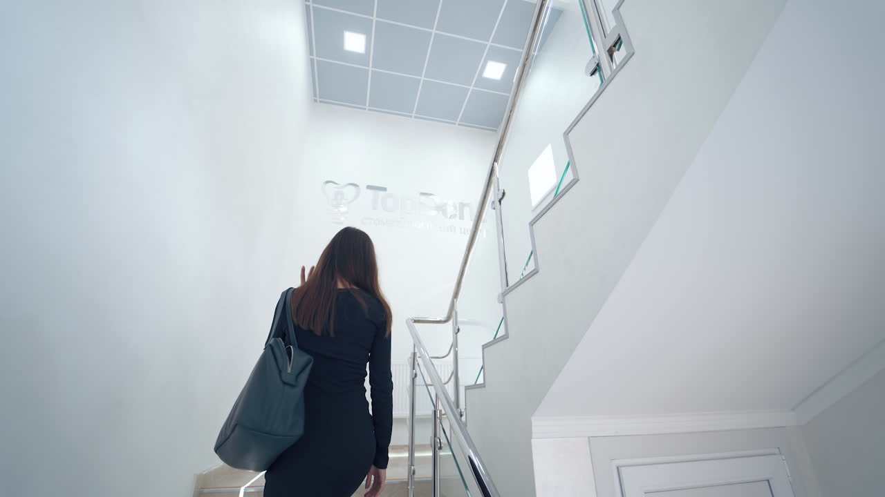 Kvinde indendørs på trappen. Bagfra-billede af ung kvinde, der går op ad trappen.