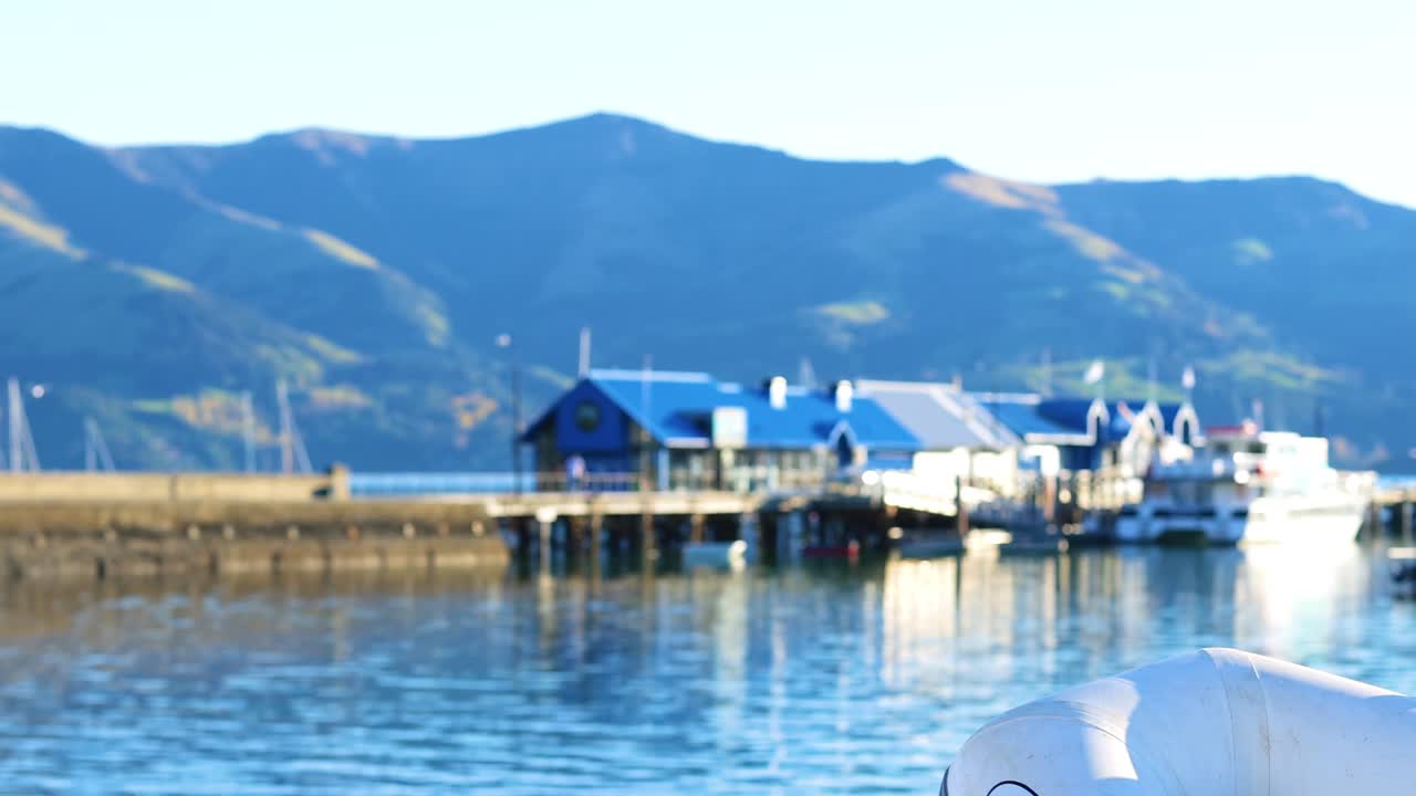 A close-up view of blue roofed structures along a tranquil waterfront with distant hills.