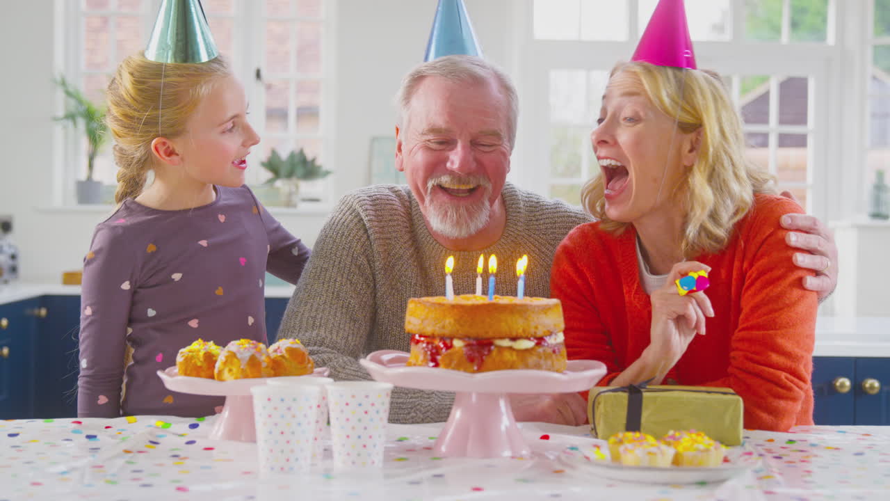 los abuelos con la nieta celebrando soplando velas en el pastel de cumpleaños en casa juntos