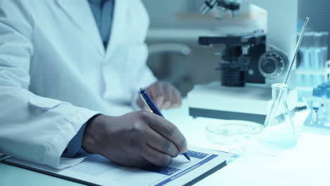 hands of male scientist working with microscope and taking notes at desk in lab